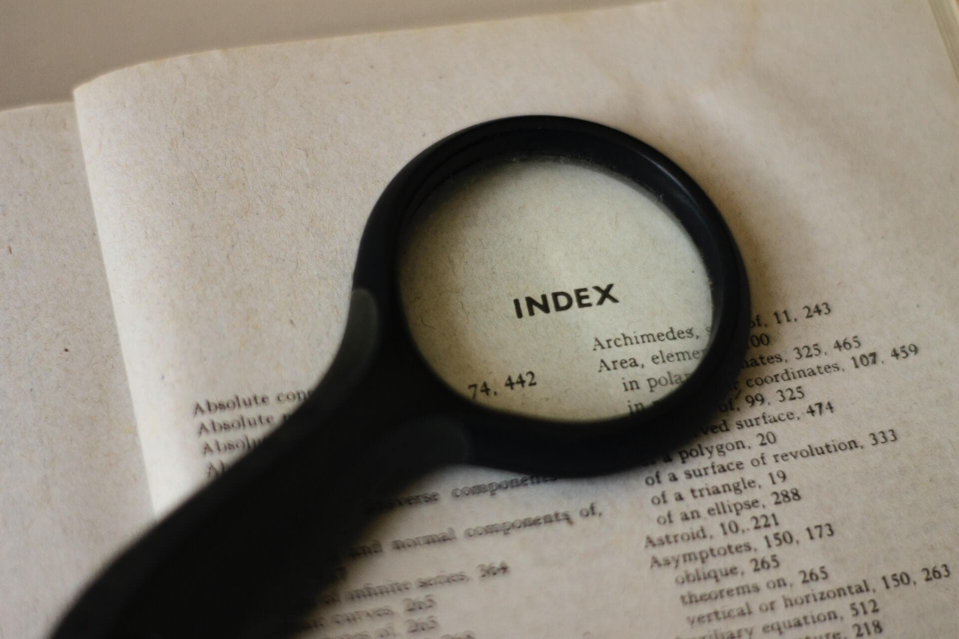 A magnifying glass over the word "indeX" on a book page