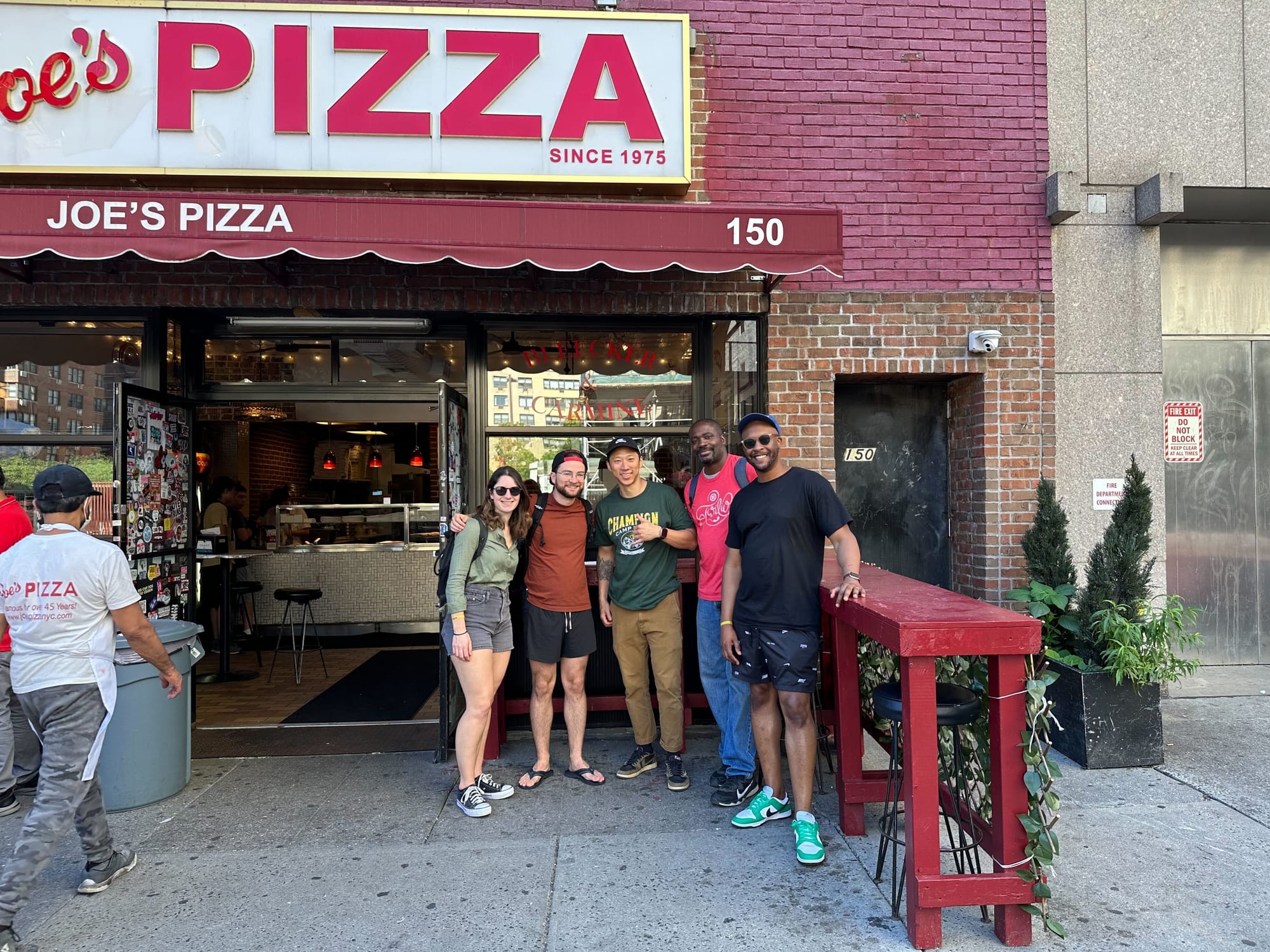 One woman and four men (part of the OpenSauced team) in front of a restaurant called Joe's Pizza